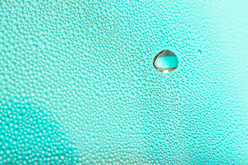 Big and small water droplets on vibrant turquoise background. The large water droplet in the upper right is in selective focus. Bokeh effect of out-of-focus droplets.