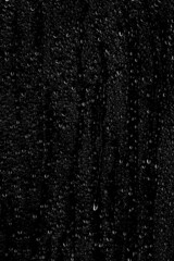 Drops of water flow down the surface of the clear glass on a black background. Vertical...