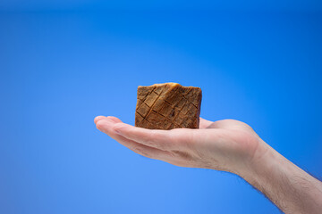 Old style homemade artisanal soap bar held in male palm. Close up studio shot, isolated on blue...