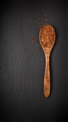 whole grain dark brown rice in a wooden spoon, also called purple rice, forbidden or chinese black rice, isolated on a black slate background, top down view with copy space
