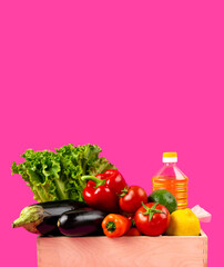 Wooden box with fresh vegetables, sunflower oil on a pink background. Delivery or donation concept. Copy space