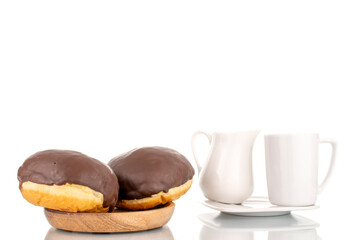 Two flavored chocolate donuts on a wooden saucer with white ceramic utensils, macro, isolated on a white background.