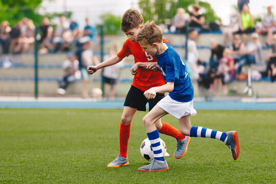 Two Kids Playing Football Ball on Grass Field. Happy School Boys Kicking Ball During Tournament Game. Children in Blue and Red Soccer Team