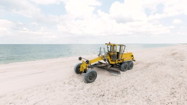 Top view of tractor on beach. Action. Bulldozer clears white beach by sea. Bulldozer clears debris or levels beach at sea