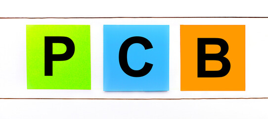 On a white wooden background there are three colorful bright stickers with text PCB Printed Circuit...