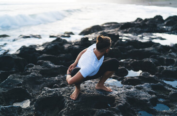 Fototapeta premium Young male in sportive wear stretching in yoga pose and meditate during morning mindfulness concentration at coastline seashore, Caucasian man enjoying hatha practice for enlightenment harmony