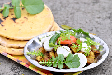 closeup the bunch sliced tomato with white radish and fried veg ,green leaves with yellow unleavened bread in the plastic tray over out of focus grey brown background.