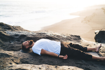 Bearded man with closed eyes lysing and resting during pastime for pranayama breathing in nature...