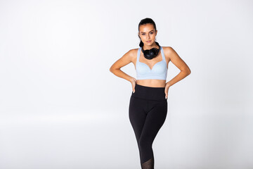 woman with headphones around her neck on white background in sport outfit with pony tail, female trainer with music gear ready for gym and workout