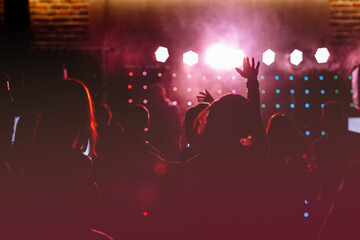cheering crowd in front of bright red stage lights. Silhouette image of people dance in disco night...