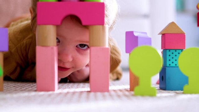 closeup of little baby playing with colorful wooden blocks, building a toy castle on the carpet at home on sunny day