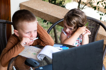 A little boy and a girl are sitting in front of a laptop. distance learning. children using technology. Children at the computer. Online training. Kids and gadgets. Siblings watch cartoons.