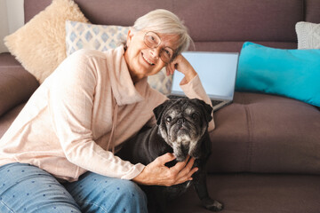 Happy couple smiling elderly woman and funny old pug dog at home sitting on sofa for family...