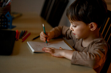 a five-year-old boy learns to draw remotely. the boy draws a drawing with colored pencils