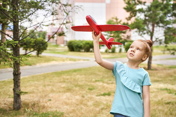 Little girl with airplane toy. Adventure fly concept. Stay home game. Family garden activity. Red...