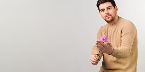 Young handsome man wearing sweater with beautiful flower holding in his hand standing over white background.