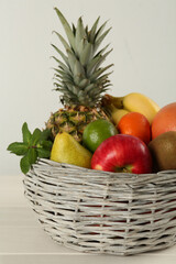 Fresh ripe fruits in wicker bowl on white wooden table, closeup