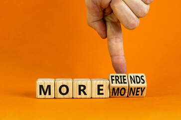 More friends or money symbol. Businessman turns wooden cubes and changes concept words More money to More friends. Beautiful orange background, copy space. Business, more friends or money concept.