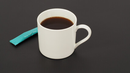 Hot coffee in white cup and white sugar sachet on black background.