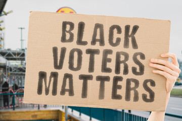 The phrase " Black voters matters " on a banner in men's hand with blurred background. Violence. Democrat. Teenager. Slogan. Social. Strike. Public. Privacy. Problem. Global. Equality. Group. Civil