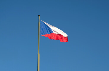National flag of the Czech Republic, tricolor of red, white and blue. The Czech flag on a flagpole flutters in the wind against a blue sky.