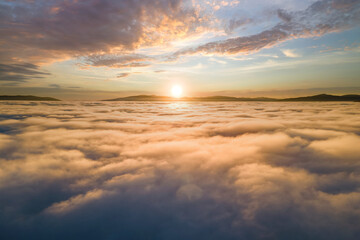 Aerial view of vibrant sunset over white dense clouds with distant dark mountains on horizon