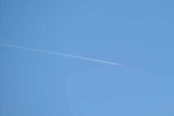 Distant passenger jet plane flying on high altitude on clear blue sky leaving white smoke trace of contrail behind. Air transportation concept