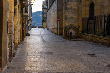 Fototapeta na wymiar Calle 31 de Agosto, old part, old neighborhood, old city of San Sebastián Donostia, a cold winter morning, at dawn, you can see the empty street, the streetlights on, the shiny ground and the awakenin