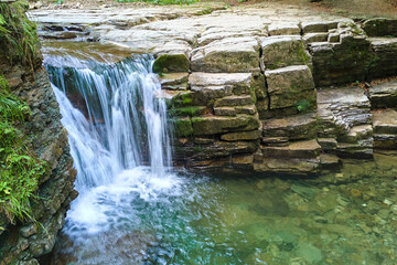Waterfall on mountain river with white foamy water falling down from rocky formation in summer forest