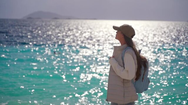 A woman walks along the beach with a camera. Beautiful azure sea on the background
