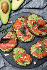 Delicious sandwiches with salmon, avocado and herbs on grey table, flat lay