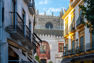 View of the Seville Cathedral through an alley street with buildings on either side in the Barrio Santa Cruz district of Seville, Spain.
