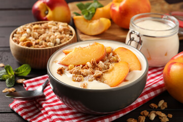 Tasty peach yogurt with granola and pieces of fruits in bowl on wooden table