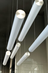 Modern design of lamps in the interior on the false ceiling of the hall. Volumetric composition of long cylindrical white fluorescent lamps.