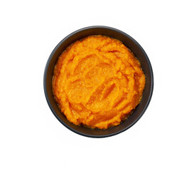 Pumpkin puree (mashed butternut squash) in black ceramic bow isolated on a white background.