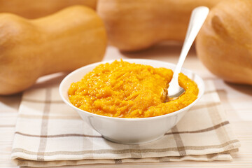 Bowl of homemade puree with organic pumpkin butternut squash on a white wooden table, selective focus.