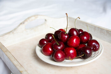 A ripe cherry in a saucer is on a wooden tray on a light background. Fresh and beautiful cherry berries are on a plate.