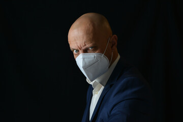 A man in a business suit with a medical mask on his face on a black background. Means of protection of respiratory organs. Precautions against infection with Covid-19 (SARS-CoV-2).