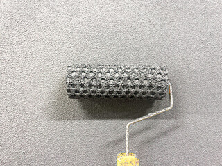 Paint roller paints the wall with structural paint