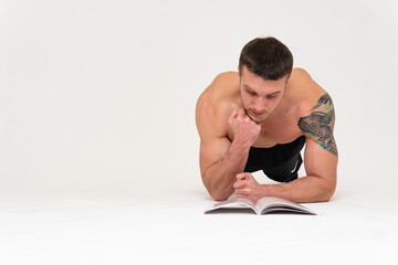 Obraz premium Bodybuilder reads the book on a white background isolated at the bottom of his head on his hands bodybuilder reading, muscle glasses chest muscles, sexy fit. Health winner gym, vision tan