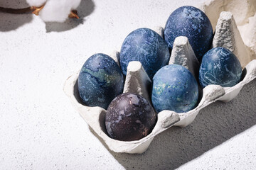 Blue easter eggs dyed with hibiscus tea in an egg carton on a white concrete background