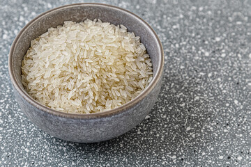 raw dry rice in a ceramic bowl on a grey plastic surface