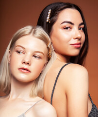 two pretty diverse girls happy posing together: blond and brunette, caucasian and asian on brown background, lifestyle people concept