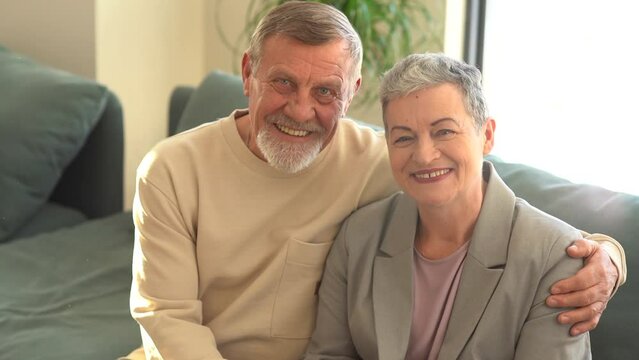 Close portrait of smiling elderly husband and wife looking at camera. A woman with a stylish short haircut and a man with a beard. Happy elderly couple