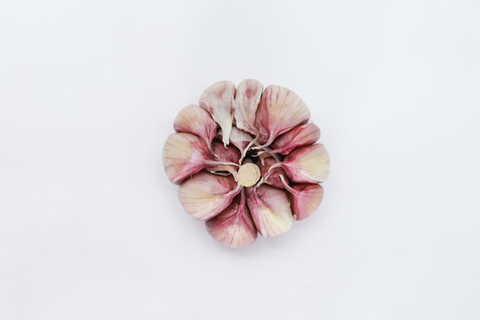 A head of garlic (Allium sativum), seen from above, slightly peeled, each clove can be seen in pinkish tones on the edges and on a neutral background