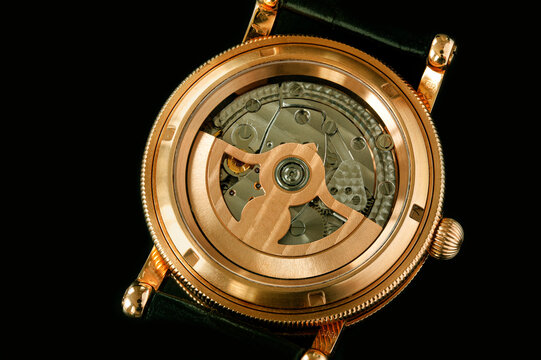 Back Of Luxury Swiss Fashion Wrist Watch Interior Mechanism With Gears And Cogs. Watch With Golden Gearwheels Gears. Vintage Movement Mechanics. Close Up Image On Black Background.