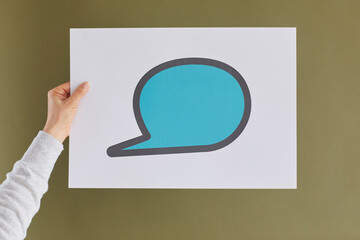 Close up of white paper with drawn blue chat message icons in hand of unknown woman on green background. Concept of communication via messengers and social media.