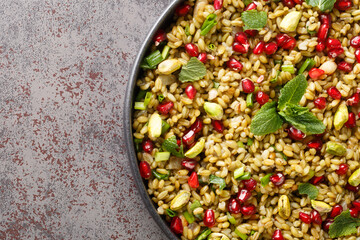 Boiled freekeh with pomegranate, nuts and herbs close-up in a plate on the table. horizontal top view from above
