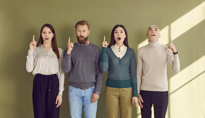 Group of people struck by an amazing idea. Team of 4 people standing in line and pointing their index fingers up happy that they managed to think of such a great, clever idea