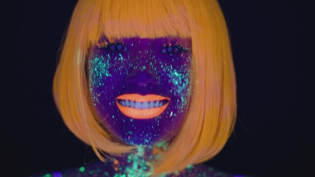 Neon beauty. Close up portrait of young pretty lady with bright glowing fluorescent makeup smiling to camera